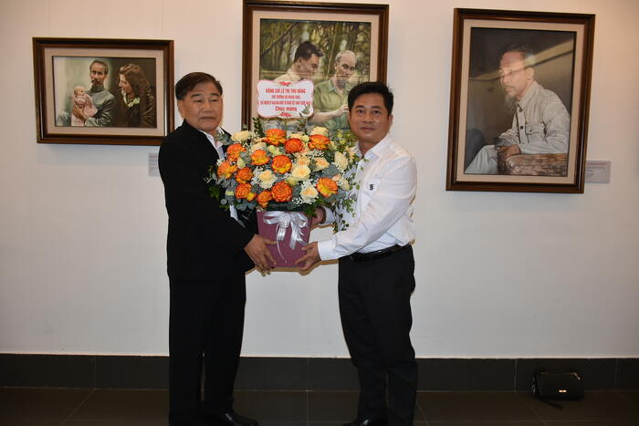 Ông Đinh Hoàng Linh - Vụ trưởng Vụ Pháp chế Thanh tra, Ủy ban Nhà nước về NVNONN - chuyển lẵng hoa chúc mừng của Thứ trưởng Lê Thị Thu Hằng tới họa sĩ Đào Trọng Lý