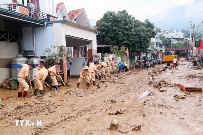 Lực lượng Cảnh sát giao thông tham gia thu gom bùn đất, cành cây, rác bị tràn về trong đợt lũ vừa qua tại xã Sông Mã, Sơn La. (Ảnh: Quang Quyết/TTXVN) ttxvn-mua-lu-son-la-13.jpg