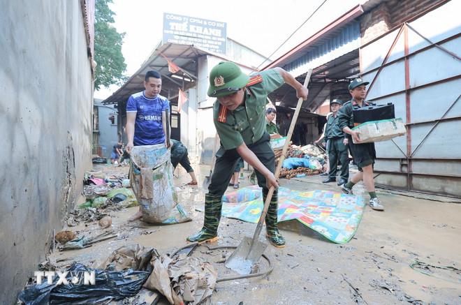 Các chiến sỹ khẩn trương thu gom rác, quét dọn bùn đất tại thôn Sông Công, xã Trung Giã, Hà Nội. (Ảnh: Lê Đông/TTXVN) ttxvn-cong-an-ha-noi-ho-tro-nhan-dan-khac-phuc-hau-qua-sau-anh-huong-bao-so-11-6.jpg